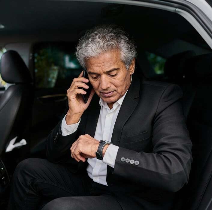 Foto di un passeggero che controlla l'ora e parla al telefono mentre è seduto sul sedile posteriore di una vettura.